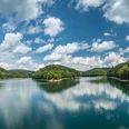 Blick auf die Aggerinsel Panorama eines Sees in Gummersbach, umgeben von bewaldeten Hügeln und reflektierenden Wolken im Wasser.