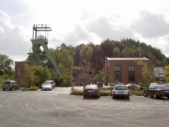 Ein stillgelegtes Bergwerksgelände mit Förderturm und Backsteingebäuden bei bewölktem Himmel.