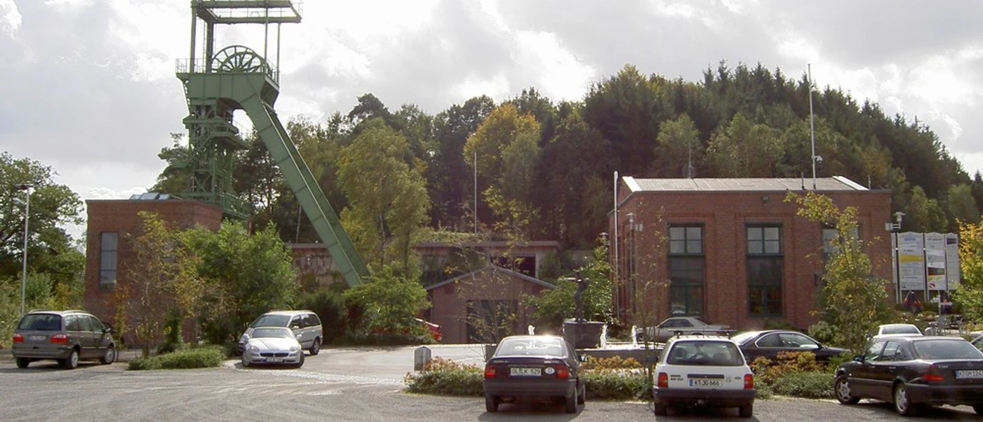 Mediendatei Ein stillgelegtes Bergwerksgelände mit Förderturm und Backsteingebäuden bei bewölktem Himmel.