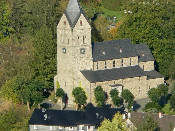 Basilika St. Gertrud Historische Kirche mit grauem Steingebäude und markantem Turm, umgeben von grünen Bäumen.