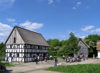 Bergisches Freilichtmuseum Lindlar Fachwerkhaus im Freilichtmuseum, Besucher auf einem Platz, umgeben von grüner Natur, blauer Himmel.
