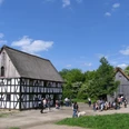 Bergisches Freilichtmuseum Lindlar Fachwerkhaus im Freilichtmuseum, Besucher auf einem Platz, umgeben von grüner Natur, blauer Himmel.