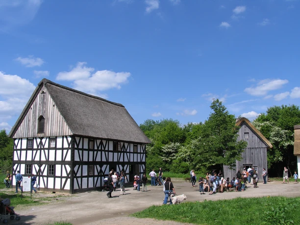 Bergisches Freilichtmuseum Lindlar Fachwerkhaus im Freilichtmuseum, Besucher auf einem Platz, umgeben von grüner Natur, blauer Himmel.