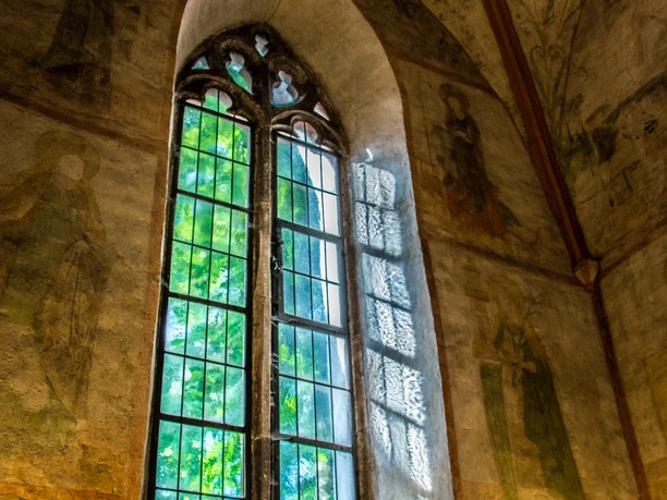 Innenansicht Gotisches Buntglasfenster mit filigranen Details und Fresken in einem historischen Gebäude, natürlich beleuchtet.