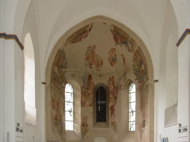 Innenansicht Heller Kirschenschiffraum mit gewölbter Decke, Altarfresken und weißen Holzbänken in historischer Kirche.