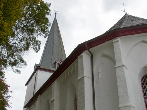 Bonte Kerke Marienhagen Weiße Kirche mit grauem Spitzdach, umgeben von Bäumen und bewölktem Himmel.