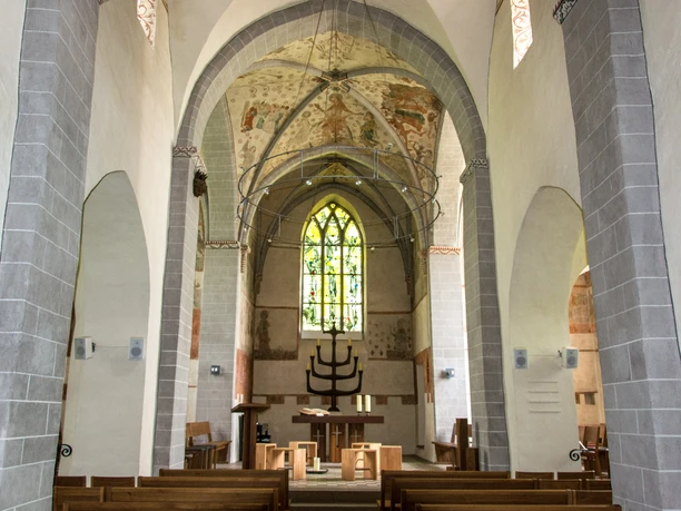 Innenansicht Historische Kirche mit hohen Gewölben, bemalten Fresken und farbigem Glasfenster im Hintergrund.