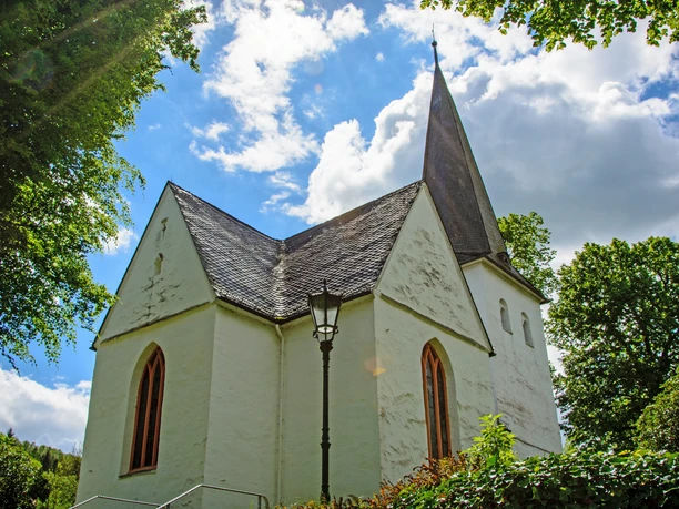 Bonte Kerke Wiedenest Weiße Kirche mit spitzem Turm in grüner Natur, umgeben von blauen Himmel und Wolken.
