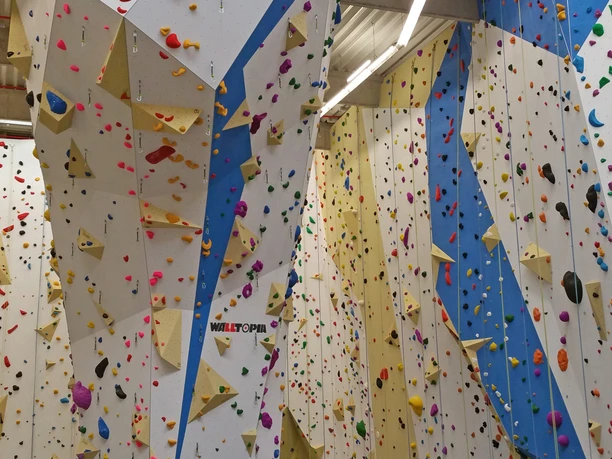 Mediendatei Moderne Kletterwand in Halle mit bunten Griffen und Routen, ideal für Indoor-Kletterer.