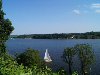 Baldeneysee Ein Segelboot fährt über den Baldeneysee in Essen an einem sonnigen, klaren Tag, umgeben von Natur.