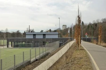 Mediendatei Ein Sportplatz mit Toren und Nebenplatz, gesäumt von Bäumen entlang eines angrenzenden Weges.