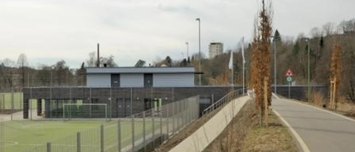 Mediendatei Ein Sportplatz mit Toren und Nebenplatz, gesäumt von Bäumen entlang eines angrenzenden Weges.