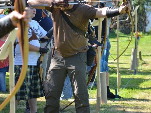 Mediendatei Männer und Jungen schießen mit traditionellen Bögen auf freiem Feld, konzentriert und zielorientiert.