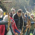 Arche e.V. Eine Gruppe von Menschen zieht Bögen bei einem Bogenschießkurs im Freien, umgeben von Natur.