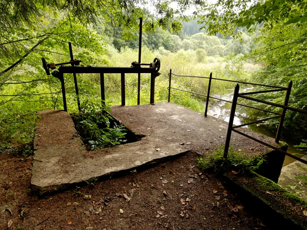 Burscheider Wehr Eine verlassene betonierte Plattform im Wald, umgeben von dichten Bäumen und einem dahinter liegenden Fluss.