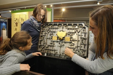 Deutsches Schloss- und Beschlägemuseum Velbert Drei Personen betrachten und erkunden das komplexe mechanische Innenleben einer historischen Truhe.