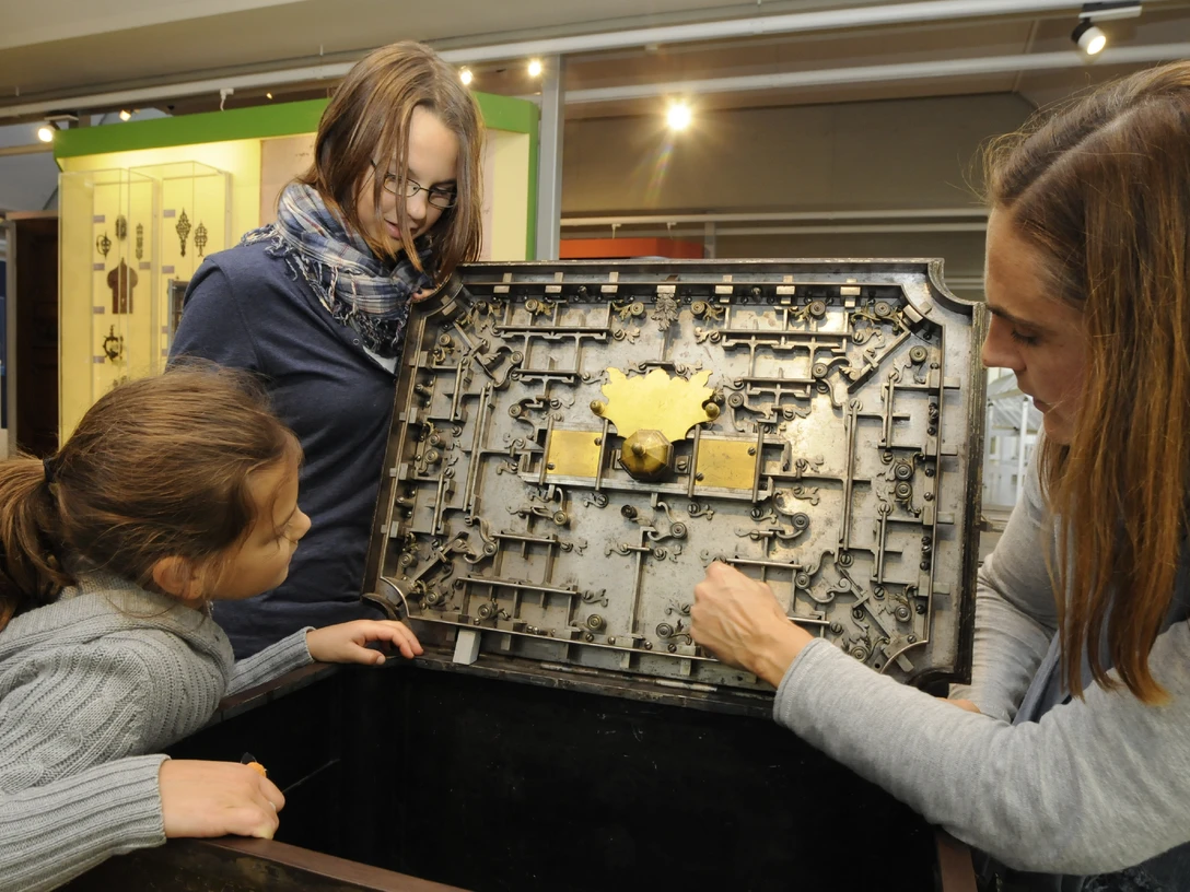 Deutsches Schloss- und Beschlägemuseum Velbert Drei Personen betrachten und erkunden das komplexe mechanische Innenleben einer historischen Truhe.
