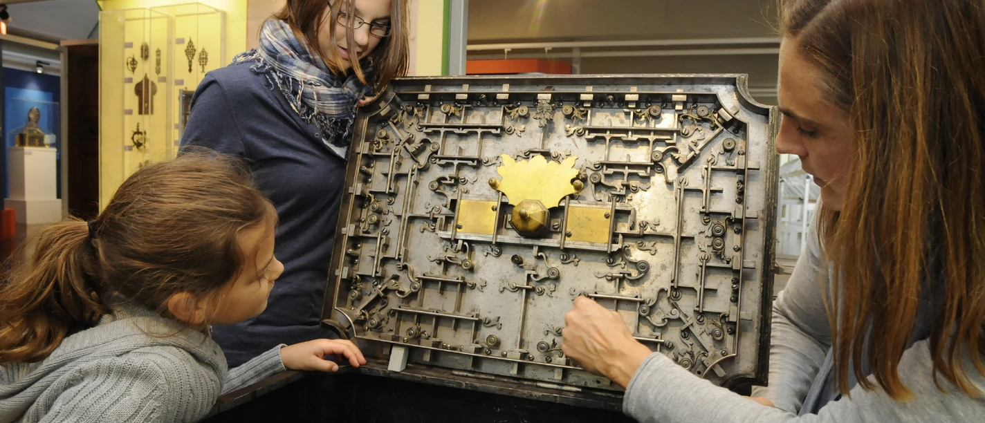 Deutsches Schloss- und Beschlägemuseum Velbert Drei Personen betrachten und erkunden das komplexe mechanische Innenleben einer historischen Truhe.