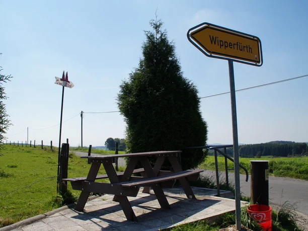 Domblick Isenburg Holzbänke und Schilder markieren eine ländliche Umgebung mit Feldern unter klarem Himmel in Wipperfürth.