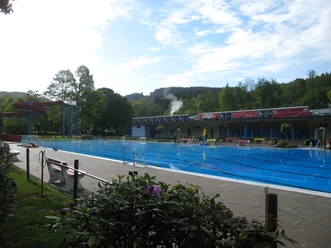 Freibad Bergneustadt Ein großes, sonniges Freibad mit langem Schwimmbecken, Wasserrutsche und umgeben von grüner Natur.