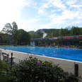 Freibad Bergneustadt Ein großes, sonniges Freibad mit langem Schwimmbecken, Wasserrutsche und umgeben von grüner Natur.