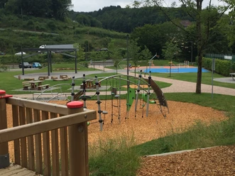 Freizeitanlage Bielstein Moderner Spielplatz mit Klettergerüst und Schaukeln, umgeben von grünen Hügeln und Bäumen.
