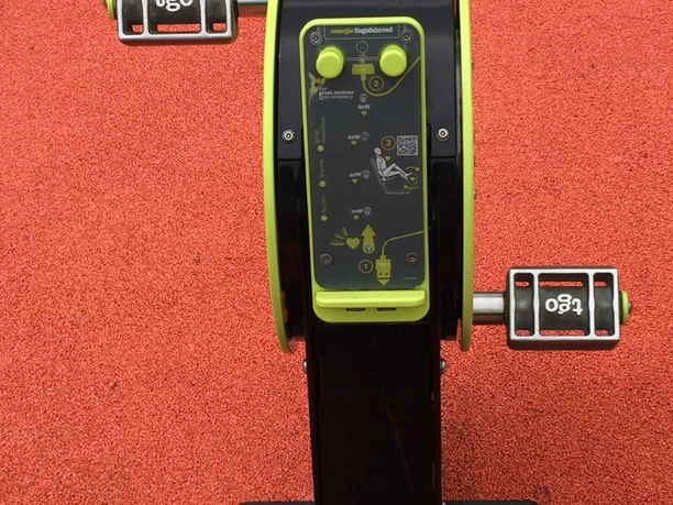 Freizeitanlage Bielstein Auf dem Bild ist ein Fitnessgerät mit Pedalen auf einem roten Gummiboden zu sehen.