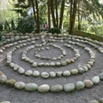 Pütz-Roth - Gärten der Bestattung Ein Steinkreis in spiralförmiger Anordnung in einem bewaldeten Gartenbereich, umgeben von Bäumen.