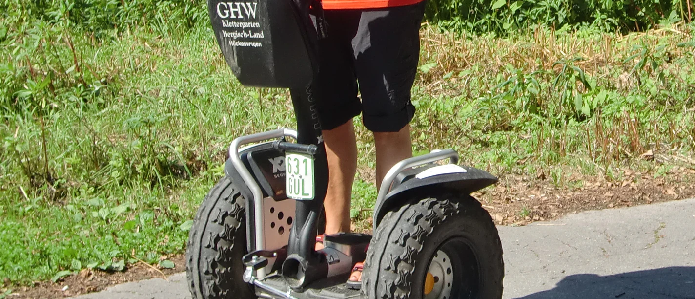 Mit dem Segway unterwegs im Bergischen Land Mann fährt auf einem Segway über einen gepflasterten Weg durch eine grüne, bewaldete Umgebung.