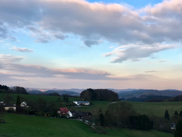 Blick über Lobscheid Idyllische Hügellandschaft mit verstreuten Häusern unter einem Himmel mit lockeren Wolken.