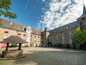 Schloss Hückeswagen Historisches Schloss in Hückeswagen mit malerischem Innenhof, flankiert von blühenden Fenstern.