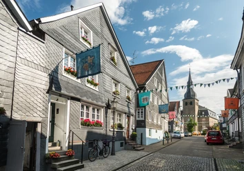 historischer Ortskern Hückeswagen <p>Schiefergedeckte Fachwerkhäuser mit bunten Wimpeln und Kirche im Hintergrund unter blauem Himmel.</p>
