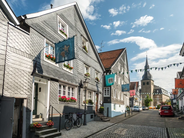 historischer Ortskern Hückeswagen <p>Schiefergedeckte Fachwerkhäuser mit bunten Wimpeln und Kirche im Hintergrund unter blauem Himmel.</p>