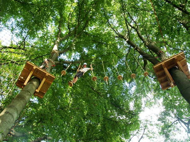 Hochseilgarten K1 Ein Kind überquert einen abenteuerlichen Seilpfad im Kletterpark, umgeben von grünen Baumkronen.