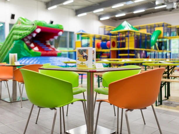 Nessi Kinderland Ein farbenfroher Innenraum eines Indoor-Spielplatzes mit bunten Stühlen und einem großen Krokodil.