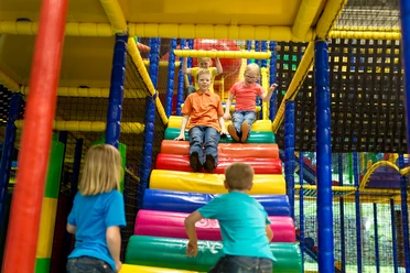 Nessi Kinderland Kinder rutschen eine bunte, überdachte Spielplatzrutsche hinunter, während andere darauf warten.
