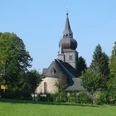 Kirche Unbefleckte Empfängnis Historische Dorfkirche mit spitzem Turm umgeben von Bäumen unter klarem, blauem Himmel.