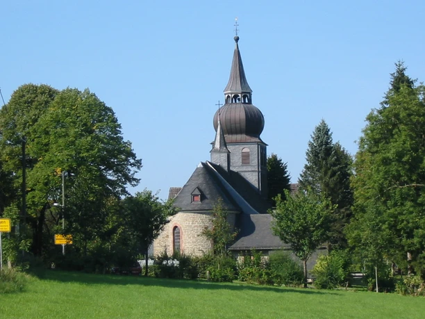 Kirche Unbefleckte Empfängnis Historische Dorfkirche mit spitzem Turm umgeben von Bäumen unter klarem, blauem Himmel.