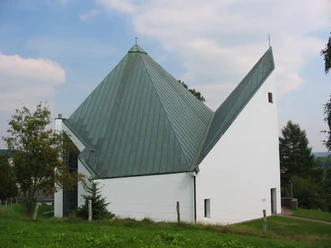 Kirche St. Anna Weiße Kirche mit markantem, grünem Metalldach; modernes Design, umgeben von Gras und Bäumen.