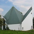 Kirche St. Anna Weiße Kirche mit markantem, grünem Metalldach; modernes Design, umgeben von Gras und Bäumen.