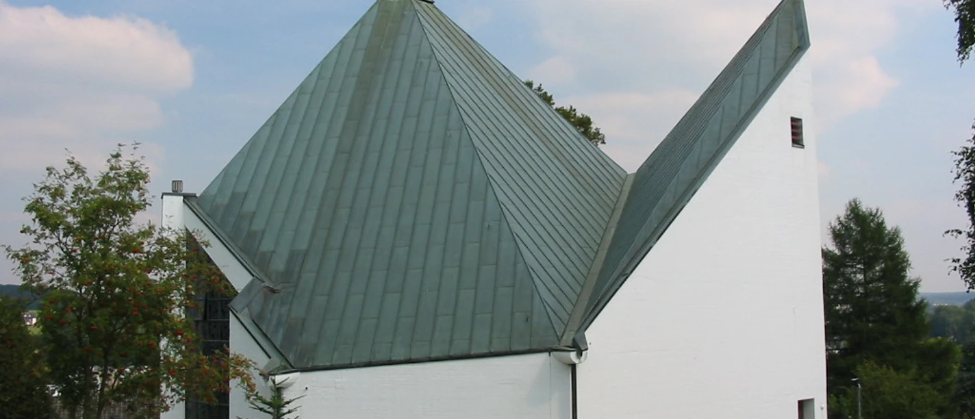Kirche St. Anna Weiße Kirche mit markantem, grünem Metalldach; modernes Design, umgeben von Gras und Bäumen.
