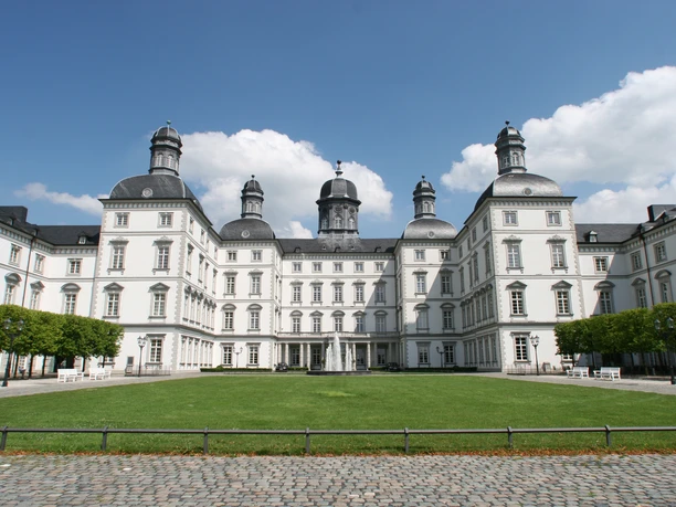 Schloss Bensberg Barockes Schloss mit eleganter Fassade, vier Türmen und gepflegtem Rasen, unter blauem Himmel.