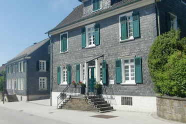Schieferhäuser im Nümbrechter Ortskern Fachwerkhaus mit grauem Schiefer, grünen Fensterläden in Nümbrecht, bei klarem Himmel fotografiert.