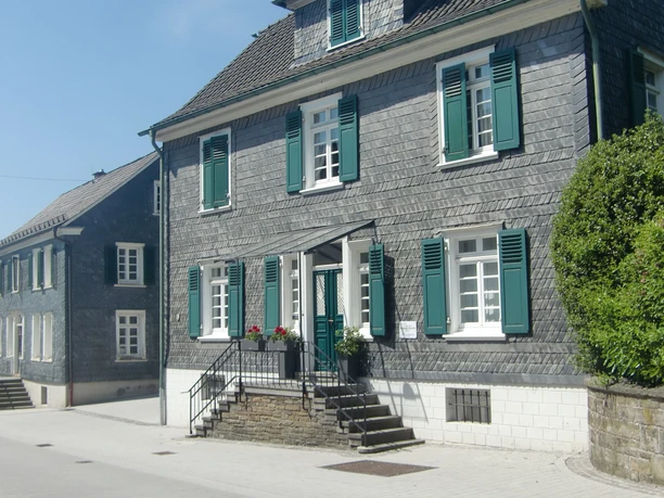 Schieferhäuser im Nümbrechter Ortskern Fachwerkhaus mit grauem Schiefer, grünen Fensterläden in Nümbrecht, bei klarem Himmel fotografiert.