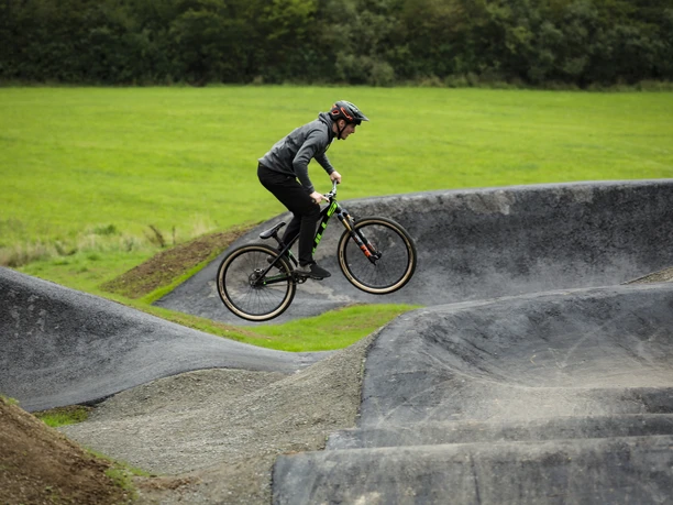 Pumptrack in Reichshof Eckenhagen Ein Jugendlicher springt mit einem Mountainbike in einem Pumptrack-Park über wellenartige Hügel.