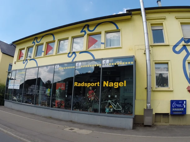 Radsport Nagel, Gummersbach Fahrradgeschäft mit gelber Fassade und großem Schaufenster, in dem Fahrräder ausgestellt sind.