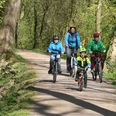 Strundeweg Eine Familie mit zwei Erwachsenen und drei Kindern fährt lachend auf Fahrrädern einen Waldweg entlang.