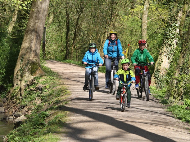 Strundeweg Eine Familie mit zwei Erwachsenen und drei Kindern fährt lachend auf Fahrrädern einen Waldweg entlang.