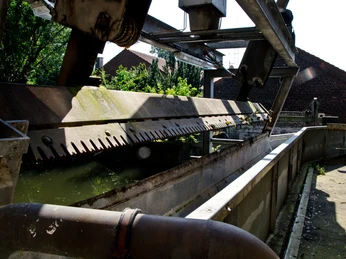 Reuschenberger Mühle Reinigungsmaschine Blick auf eine industrielle Kläranlage mit Metallstrukturen, Schatten und umgebender Vegetation.