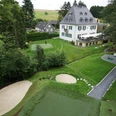 Short Game Area Eine historische Villa umgeben von grüner Landschaft und einem gepflegten Golfplatz mit Sandbunker.